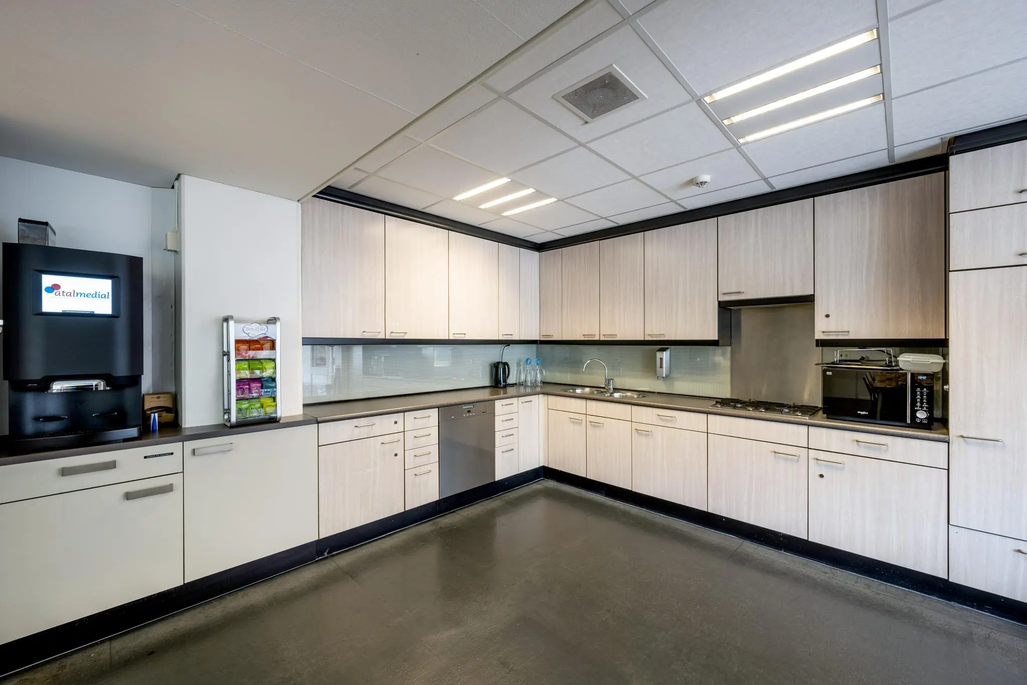 Moderne bedrijfskeuken aan de Jan Tooropstraat met lichte houten kastjes, een koffieautomaat en diverse keukenapparatuur.